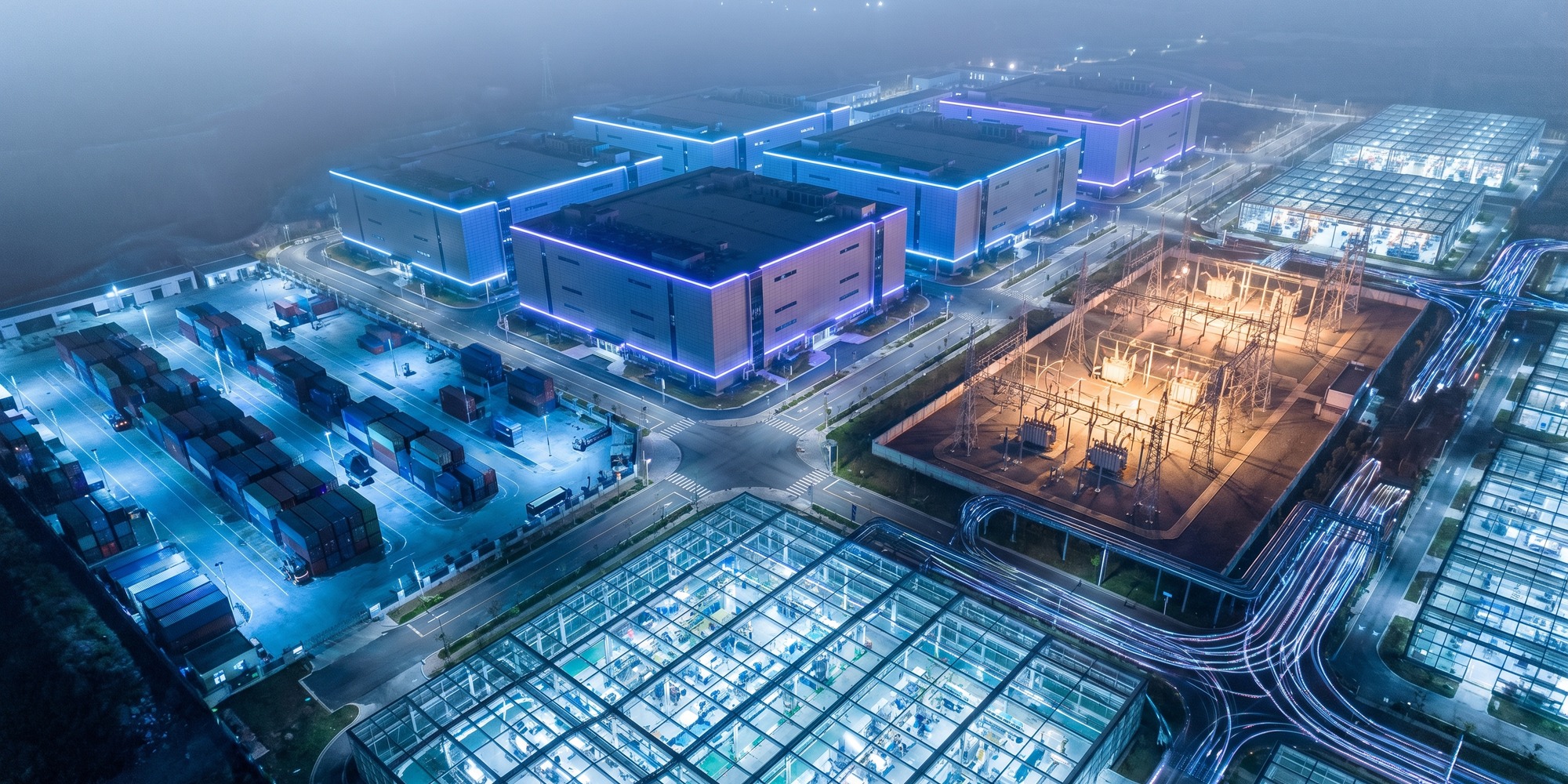 A sprawling high-tech industrial campus with hyperscale data centers, substations, and automated logistics infrastructure illuminated at night