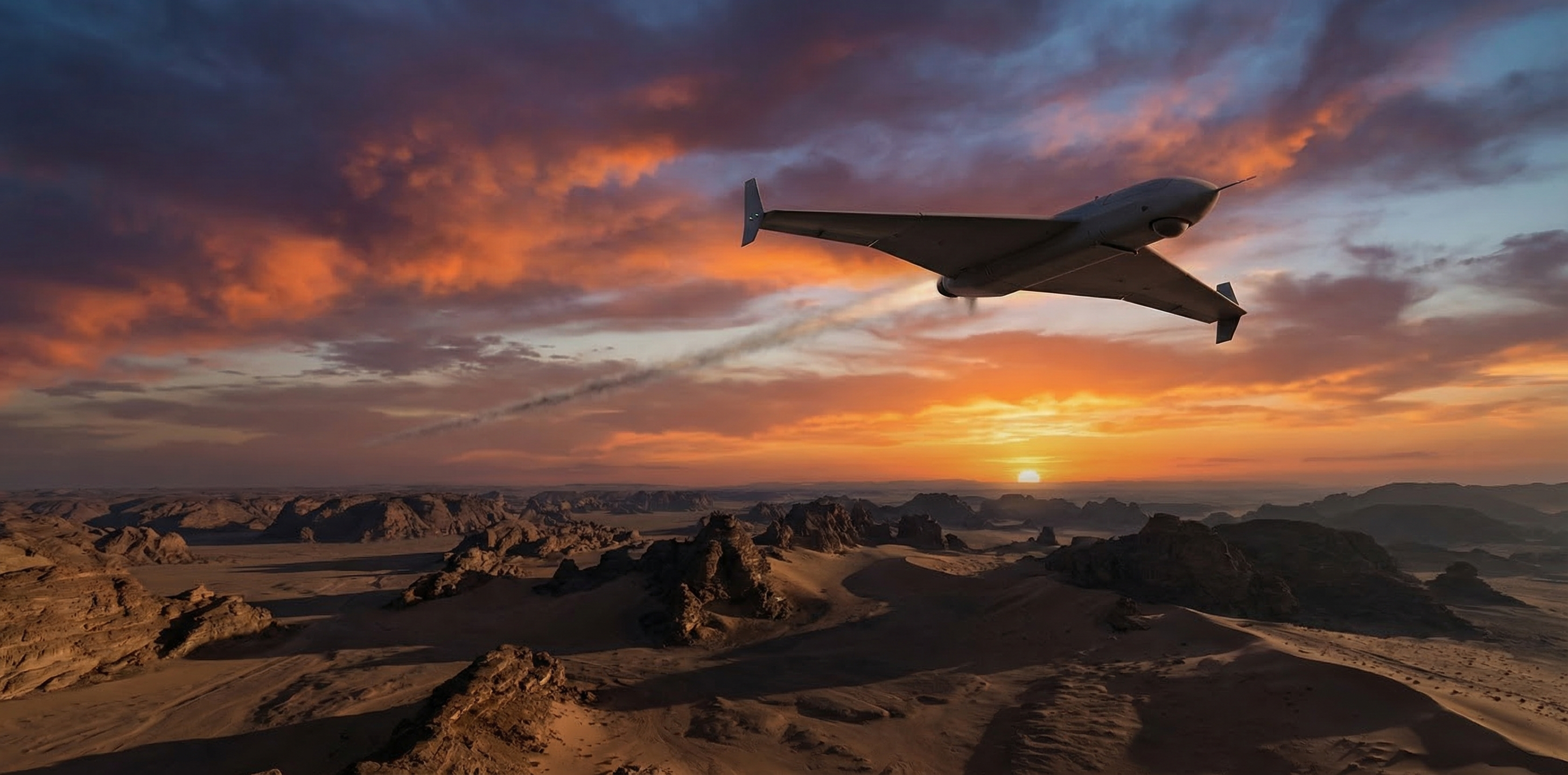 Delta-wing loitering munition drone in flight over arid desert terrain at dusk, triangular fuselage with small vertical stabilizers at wingtips, orange and purple twilight sky