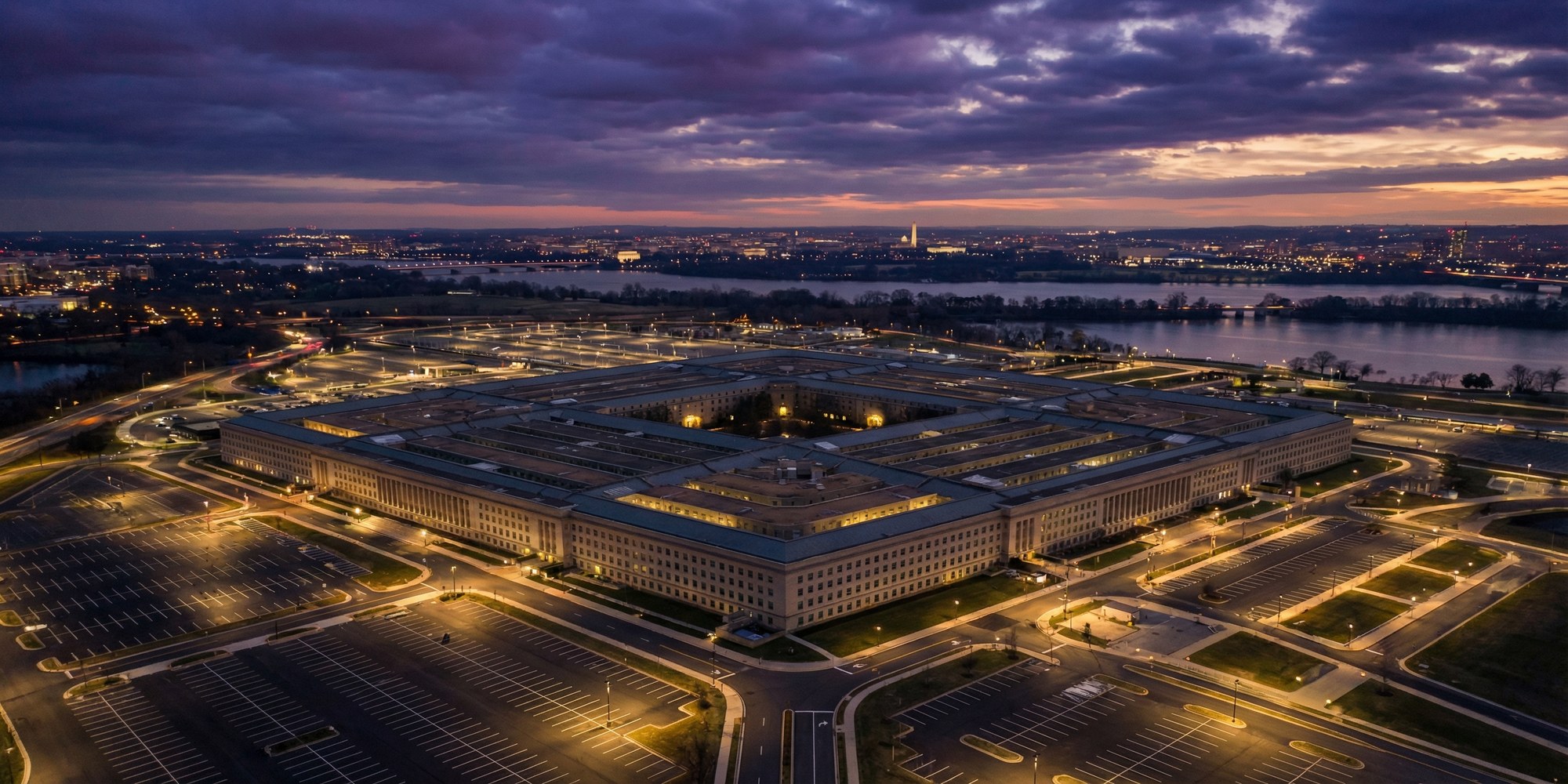 Pentagon building exterior at dusk with digital data streams and classified document folders rendered as glowing holographic overlays above the structure