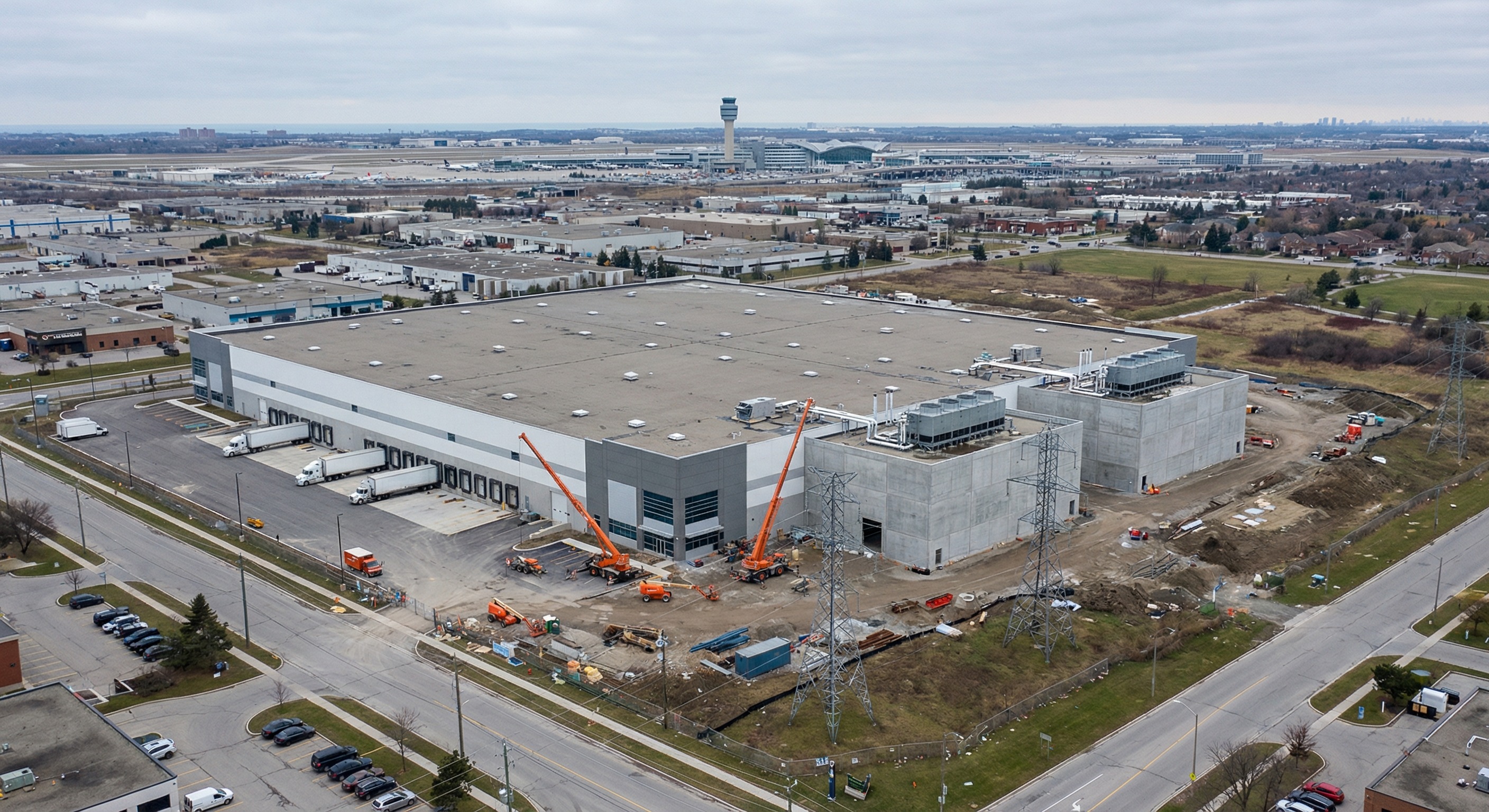 Aerial view of a large industrial warehouse complex in Mississauga Ontario being converted and expanded into a modern AI data center campus with server hall additions, surrounded by highway infrastructure and blue-grey sky