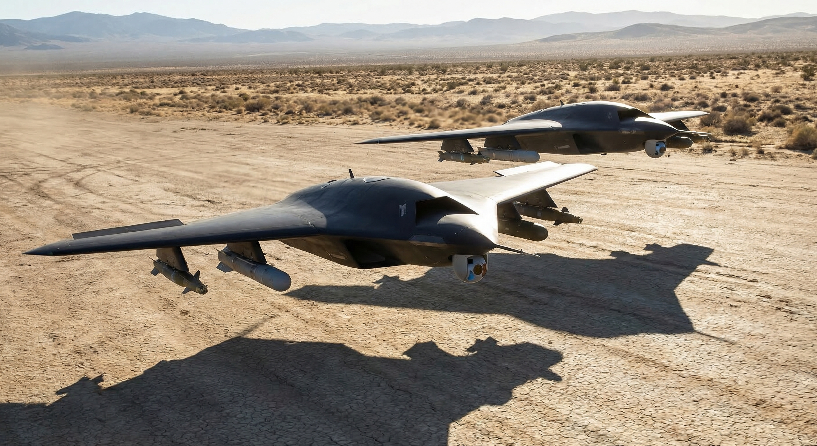 Two autonomous combat drones in formation flight over desert test range, external weapon pylons visible under swept wings